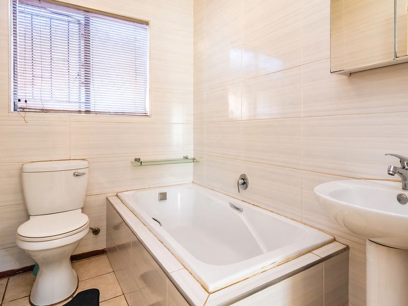 A functional bathroom featuring a built-in bathtub, pedestal basin, and toilet, finished with neutral wall and floor tiles.