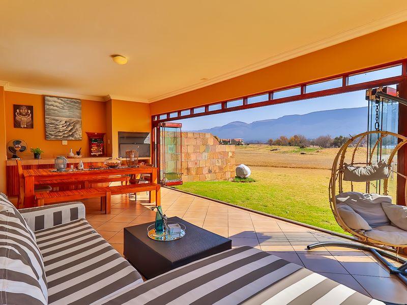Spacious covered patio featuring a built-in braai, tiled flooring, and large stacking glass doors opening to a scenic garden and mountain view.