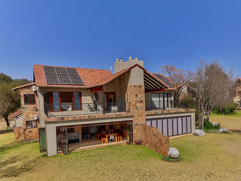 Rear view of a multi-level townhouse featuring stone cladding, terracotta roof tiles, solar panels, a spacious balcony, and a ground-floor patio with stacking doors.