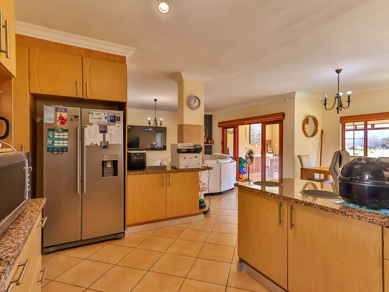 Spacious open-plan kitchen and living area featuring granite countertops, light wood cabinetry, ceramic tile flooring, and direct access to the outdoor patio.