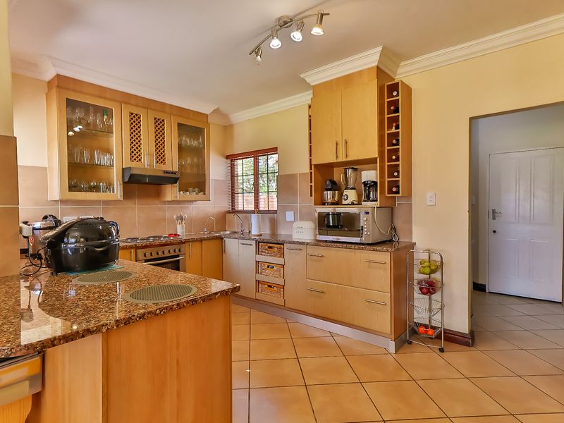 A functional kitchen featuring wooden cabinetry, granite countertops, built-in oven, hob, and tiled flooring with a neutral color palette.