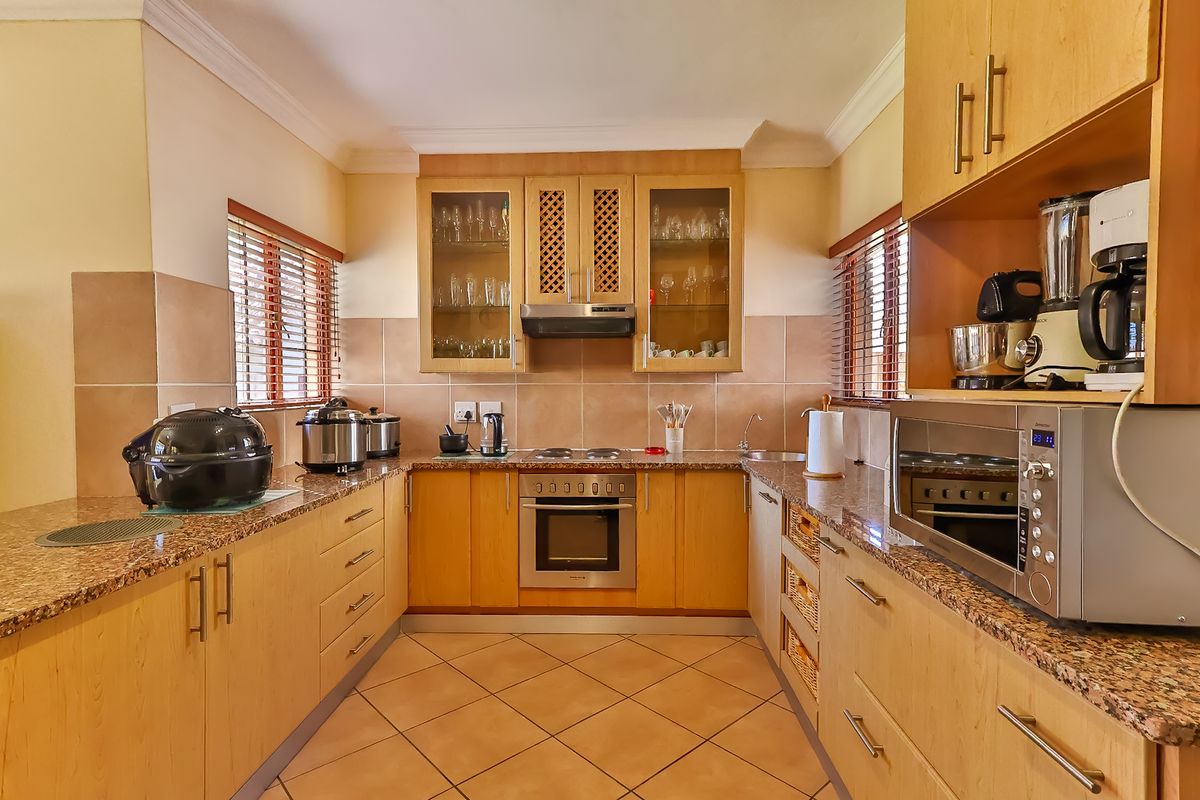 A functional U-shaped kitchen featuring light wood cabinetry, granite countertops, tiled backsplash, and integrated appliances including an oven and hob.