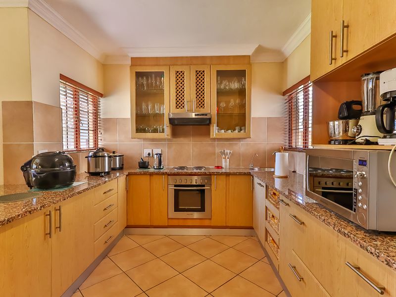 A functional U-shaped kitchen featuring light wood cabinetry, granite countertops, tiled backsplash, and integrated appliances including an oven and hob.