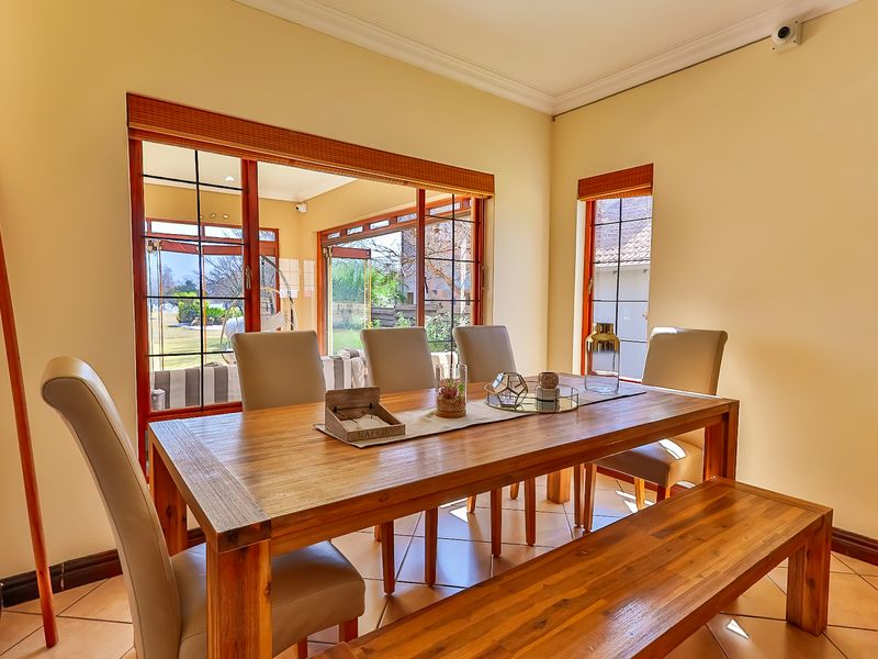 A bright dining room featuring tiled floors, timber-framed sliding doors leading to the patio, and large windows providing natural light.