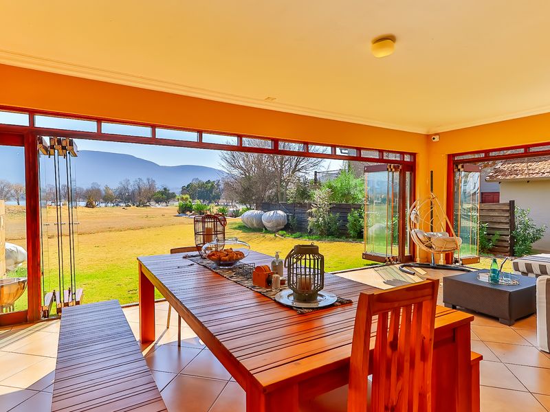 Spacious covered patio featuring large stacking glass doors that open to a scenic garden view, providing a seamless indoor-outdoor living experience.