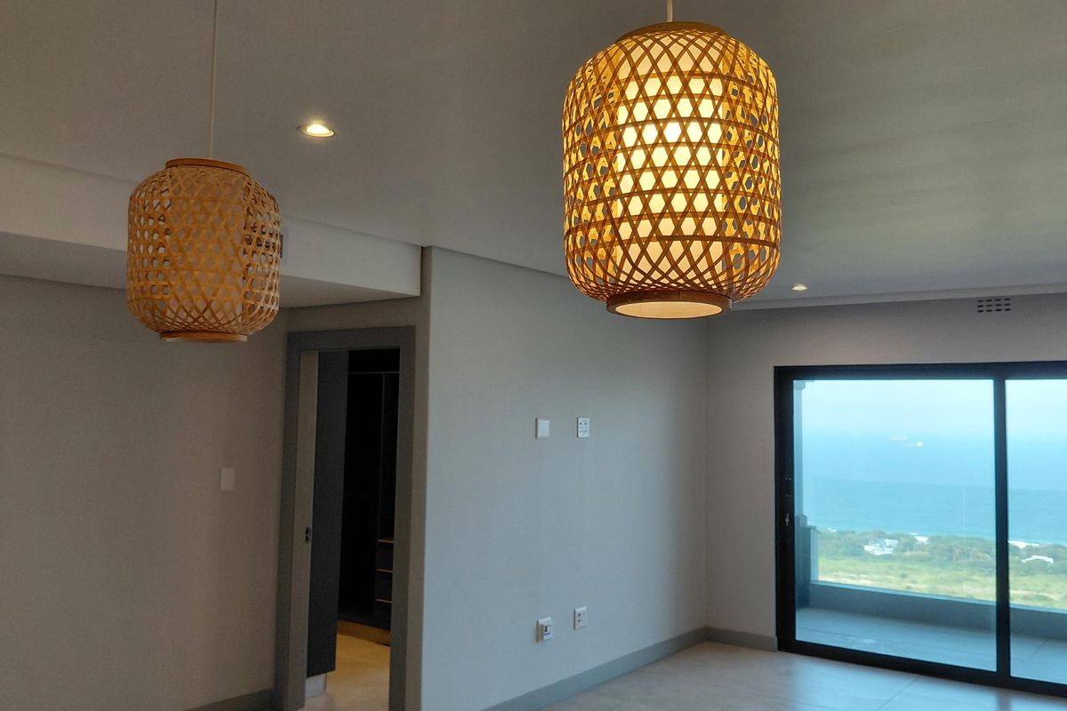 A bright living area featuring modern recessed lighting, neutral finishes, and large sliding glass doors that open to a scenic coastal view.