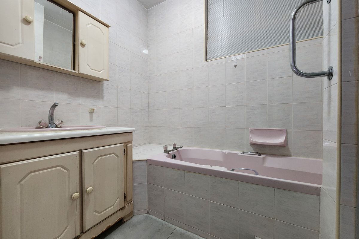 A dated bathroom featuring a pink bathtub and matching vanity basin, complete with wall-mounted grab rail and tiled wall finishes.