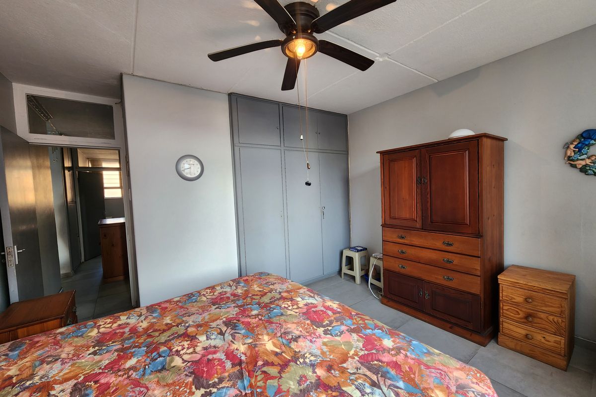 A bedroom featuring built-in grey cabinetry, a ceiling fan, and tiled flooring, providing a functional and neutral living space.