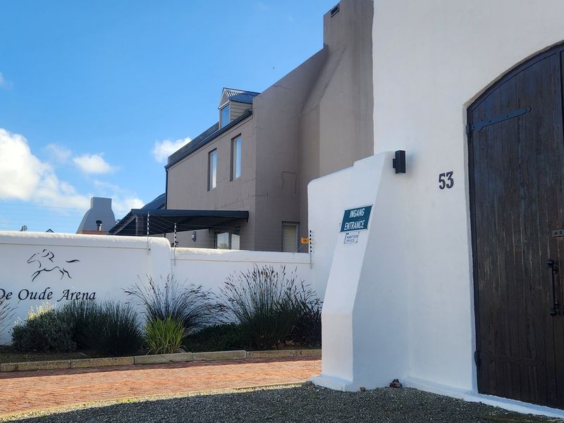 Front entrance view of the property featuring a white boundary wall, electric fencing, and large wooden double doors.