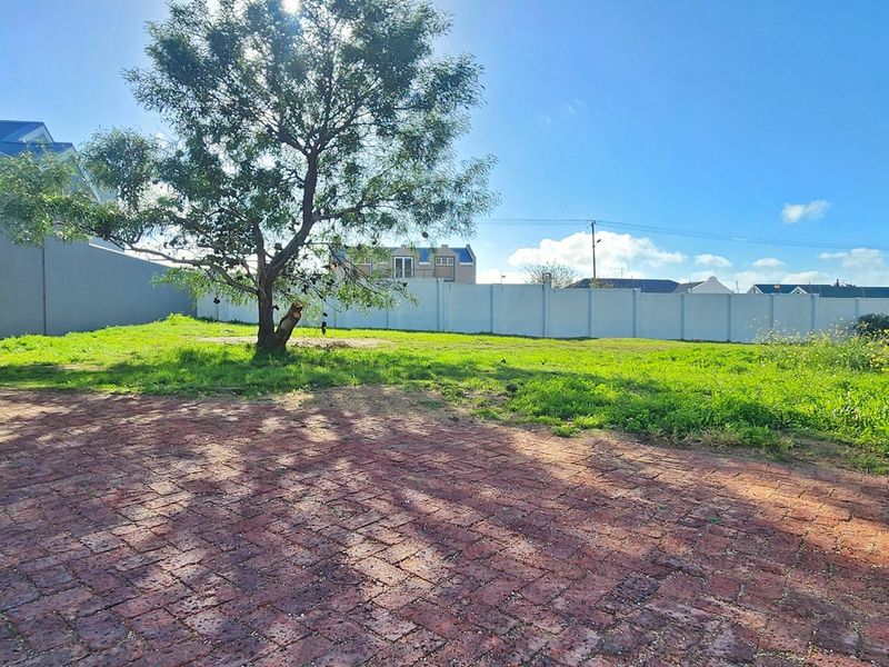 A vacant residential plot featuring brick paving, a perimeter boundary wall, and an established tree, offering a clear space for future development.
