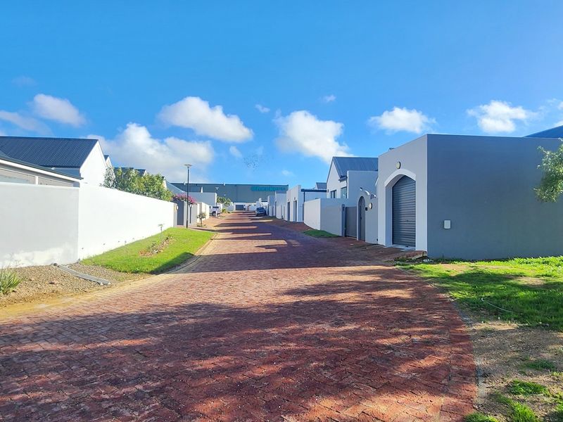 A view of a residential street featuring paved driveways, boundary walls, and modern residential architecture.