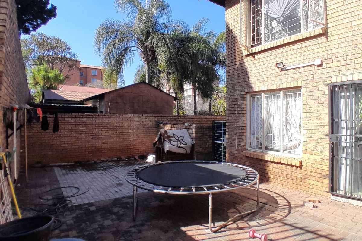 A rear exterior view of the apartment featuring a paved patio area enclosed by face brick walls and security-fitted windows.