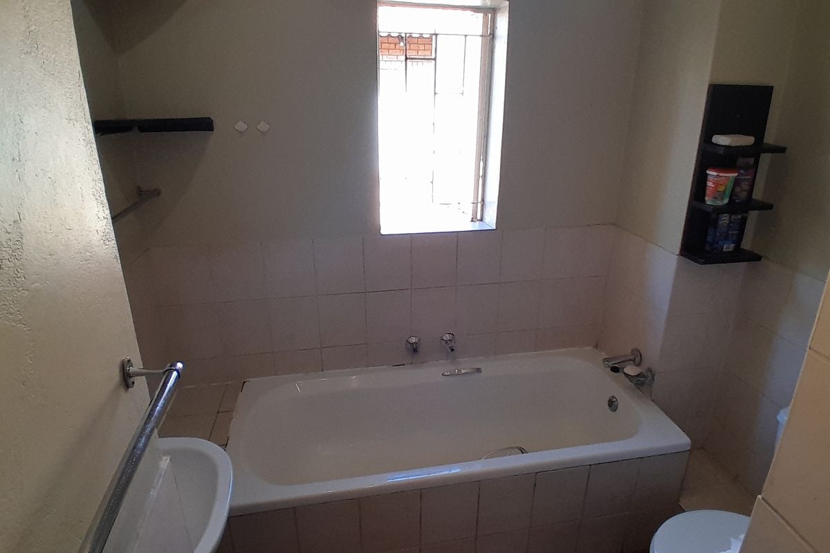 A functional bathroom featuring a built-in bathtub with tiled splashback, wall-mounted towel rail, and integrated shelving, requiring minor cosmetic updates.
