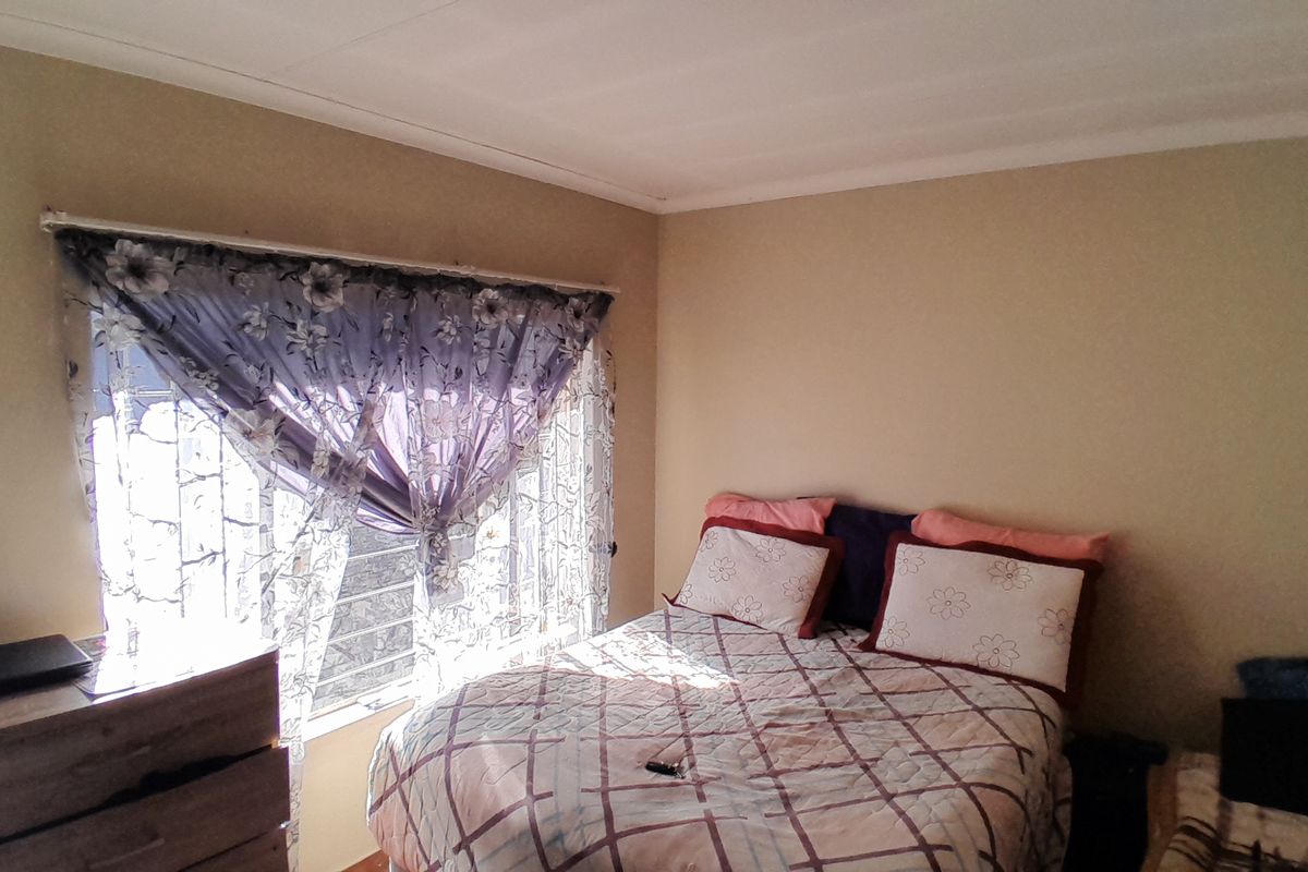 A standard bedroom featuring a window with security bars and simple cornice detailing, providing a functional space for rest.