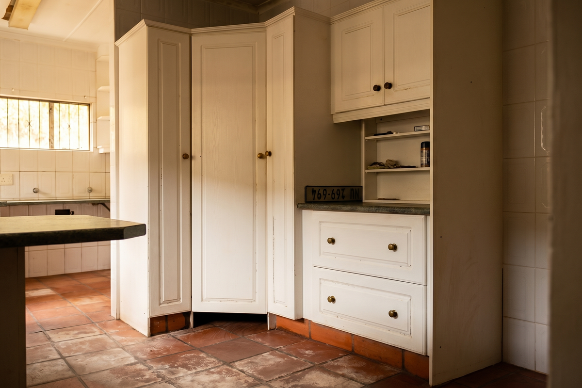 A dated kitchen featuring traditional white cabinetry, tiled flooring, and a breakfast bar, offering a functional layout ready for modernization.