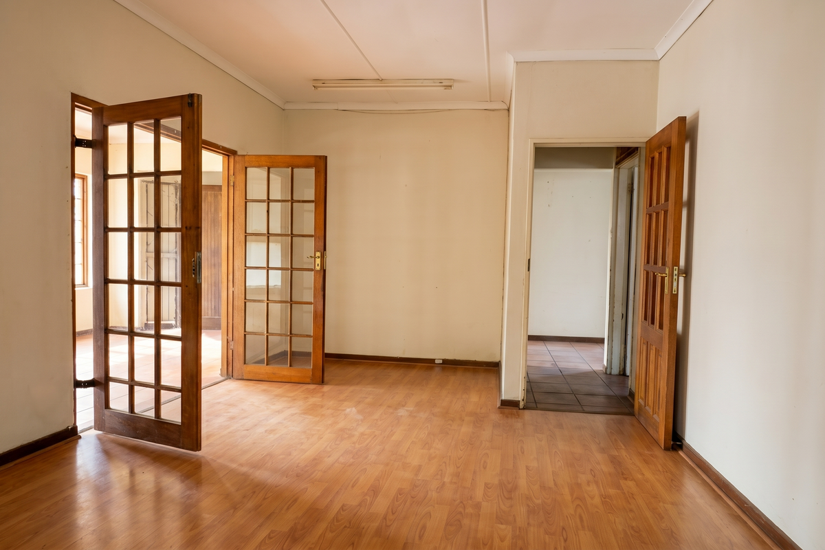 An empty living room featuring wood-look laminate flooring and traditional timber-framed glass doors leading to adjacent spaces.