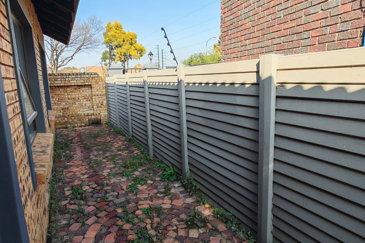 A side exterior walkway featuring brick paving and a tall precast concrete boundary wall, providing a private outdoor transition space.