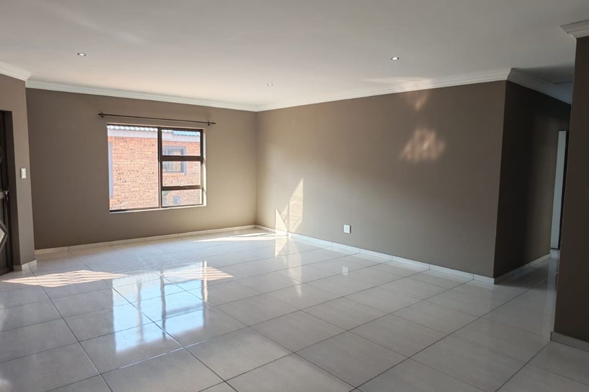 A spacious, empty living area featuring neutral-toned walls, polished floor tiles, recessed ceiling lighting, and a secure entrance door.