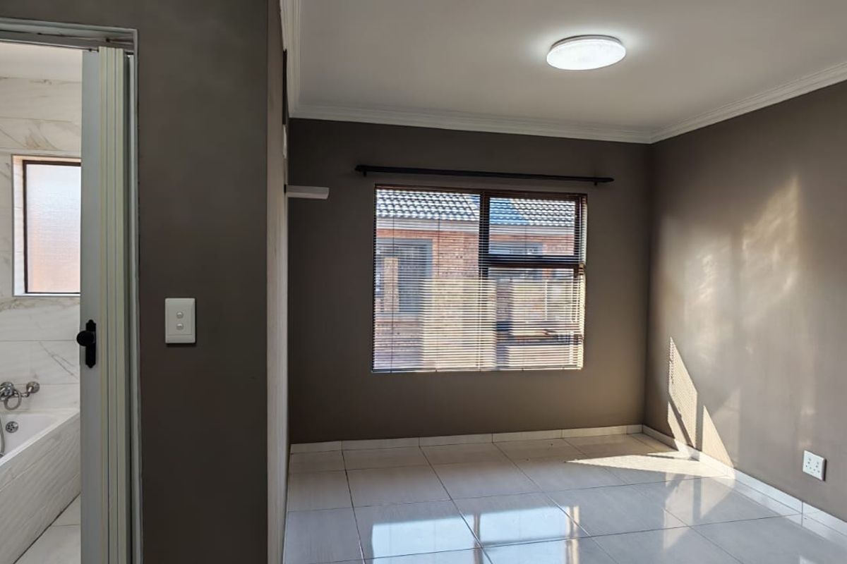 A bright bedroom featuring tiled flooring and an en-suite bathroom with modern marble-look wall tiles and a fitted bathtub.