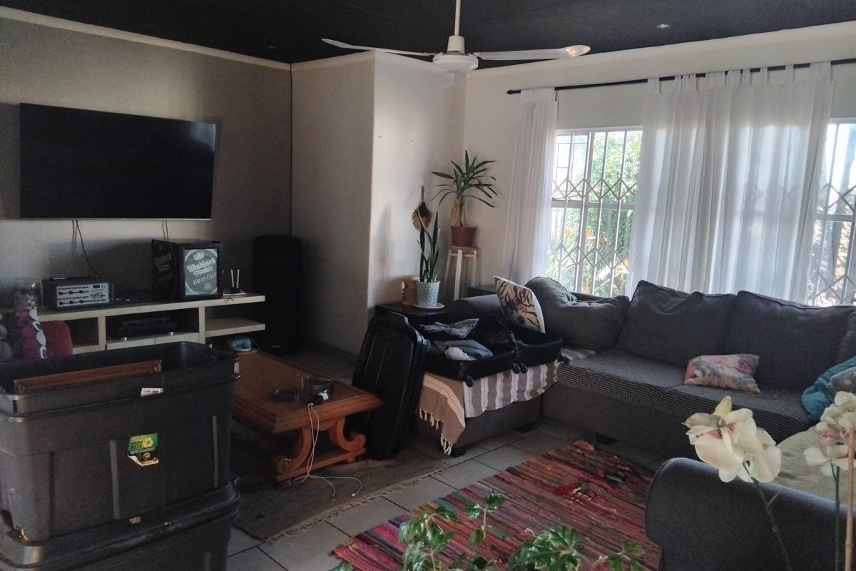 A living room featuring tiled flooring, a ceiling fan, and large windows with security gates, providing natural light to the space.
