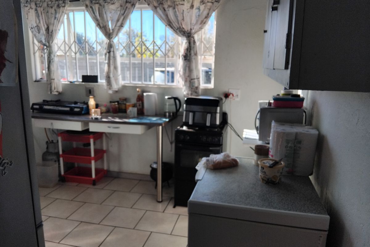A functional kitchen space featuring tiled flooring, security bars on windows, and basic cabinetry with a freestanding oven and gas hob setup.
