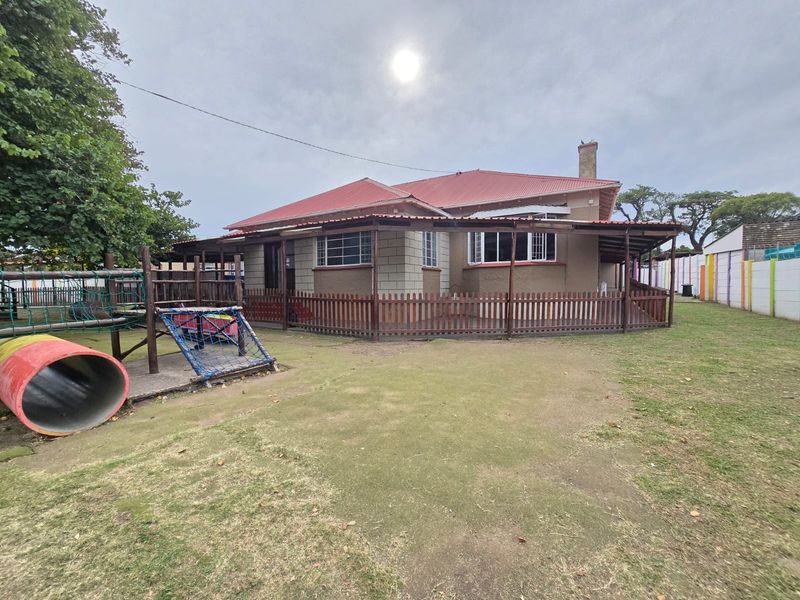 Rear view of the property featuring a covered patio area, brick and rendered exterior walls, a red metal roof, and a large garden space.