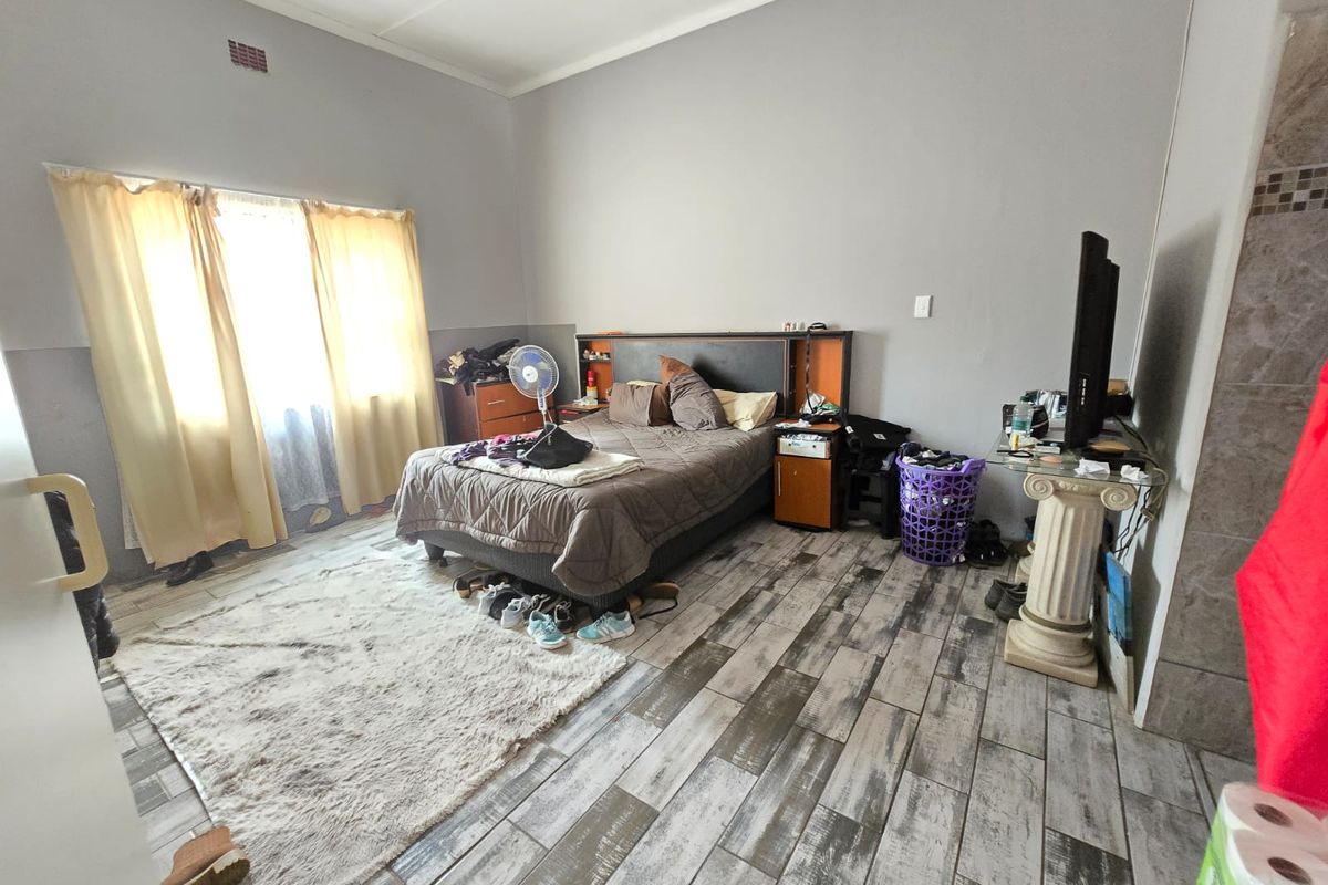 A bedroom featuring wood-look ceramic floor tiles, neutral wall paint, and a built-in headboard unit with integrated storage.