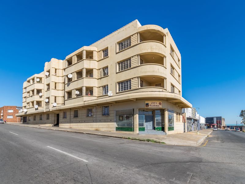 A multi-story apartment building with a corner commercial storefront, featuring curved balconies and a prominent street-facing facade in an urban setting.