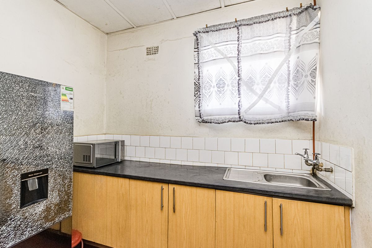A functional kitchen area featuring laminate cabinetry, a stainless steel sink, and tiled backsplash, requiring cosmetic updates to improve its overall condition.