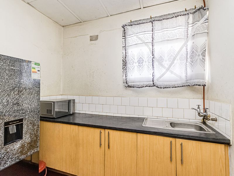 A functional kitchen area featuring laminate cabinetry, a stainless steel sink, and tiled backsplash, requiring cosmetic updates to improve its overall condition.