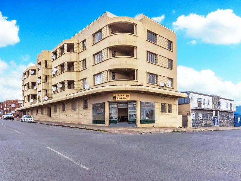 A multi-story apartment building featuring a prominent corner commercial storefront and multiple balconies, situated on a street corner.