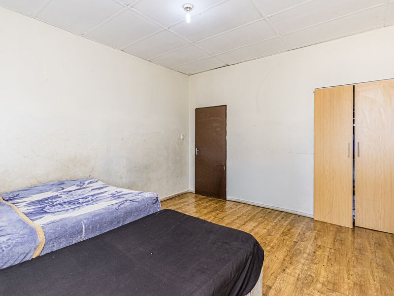 A bedroom featuring laminate flooring, a built-in wardrobe, and a drop ceiling. The walls show signs of wear and staining.