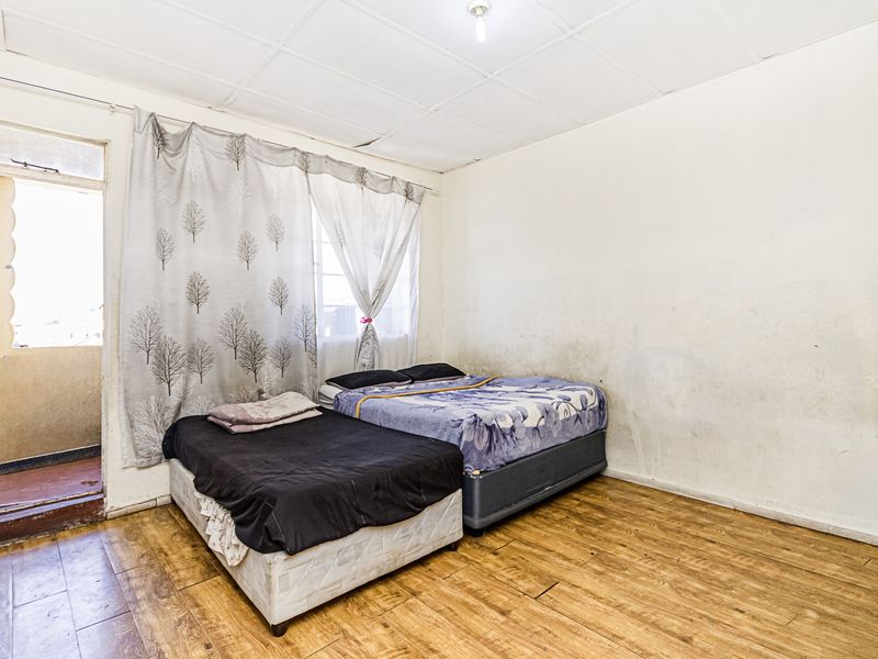 A bedroom featuring laminate flooring and direct access to a balcony, requiring cosmetic updates to the walls and ceiling.