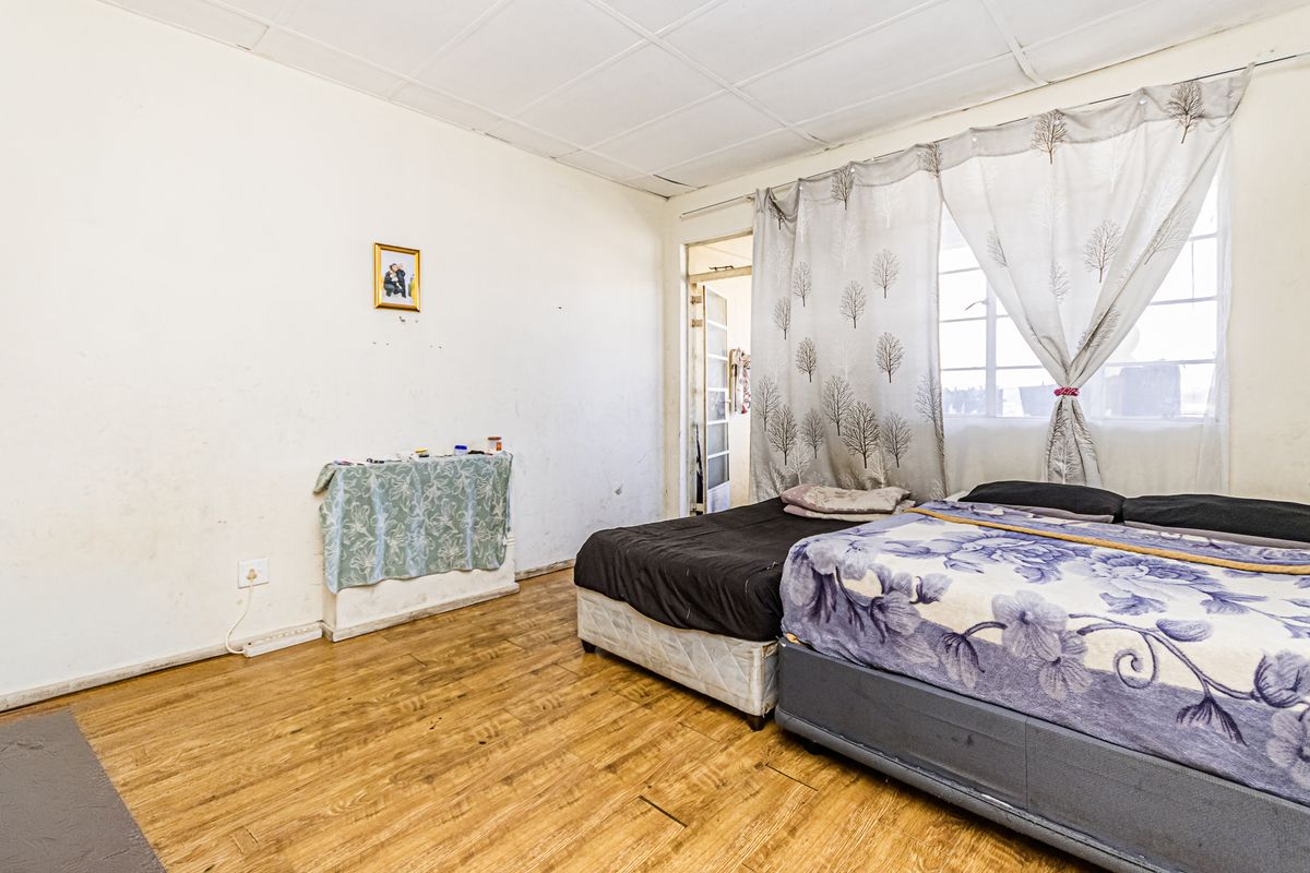 A bedroom featuring laminate flooring, a tiled ceiling, and a window with natural light. The space requires cosmetic updates to improve its overall condition.
