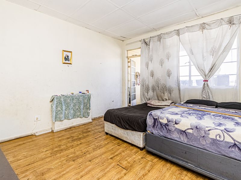 A bedroom featuring laminate flooring, a tiled ceiling, and a window with natural light. The space requires cosmetic updates to improve its overall condition.