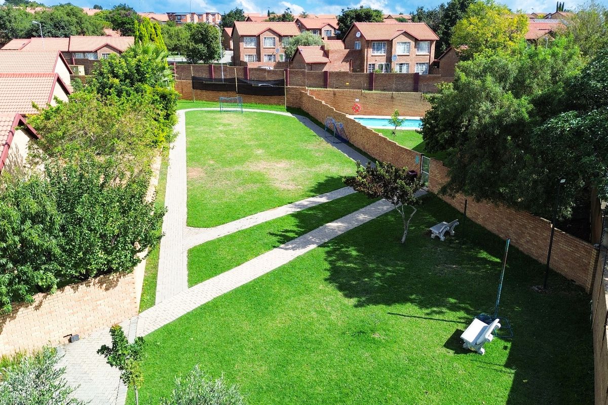 Aerial view of a communal garden area featuring paved walkways, manicured lawns, and a perimeter brick wall within a residential townhouse complex.