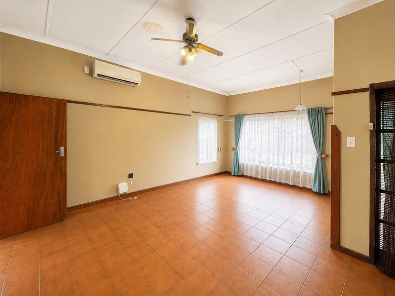 Spacious living area featuring tiled flooring, a ceiling fan, and a wall-mounted air conditioning unit, offering a neutral canvas for personalization.