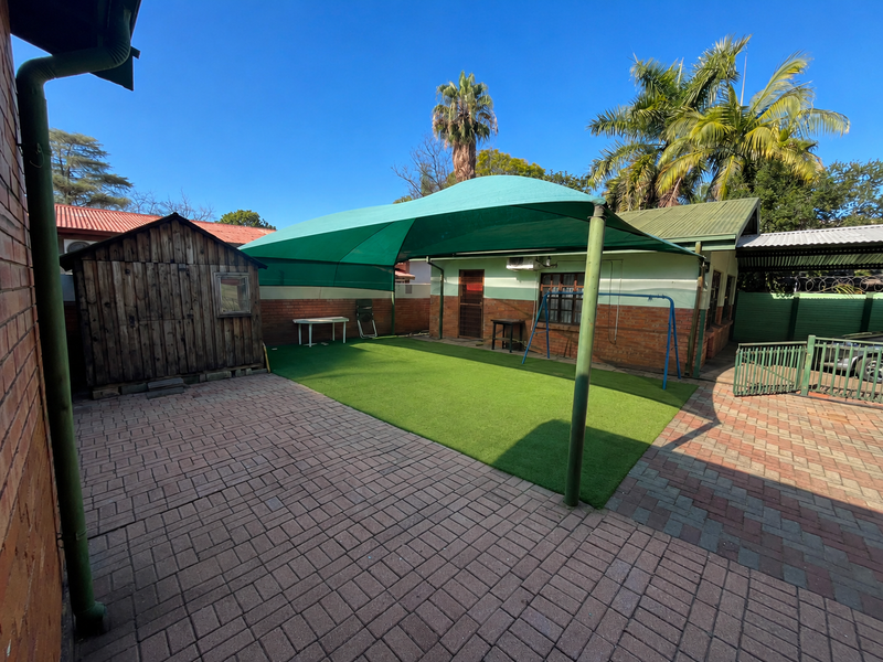 Rear courtyard featuring paved areas, artificial lawn, a large shade sail, and a timber garden shed, providing a functional outdoor entertainment space.