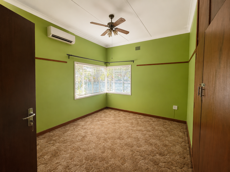 An empty bedroom featuring carpet flooring, built-in wooden wardrobes, a ceiling fan, and a split-system air conditioner.