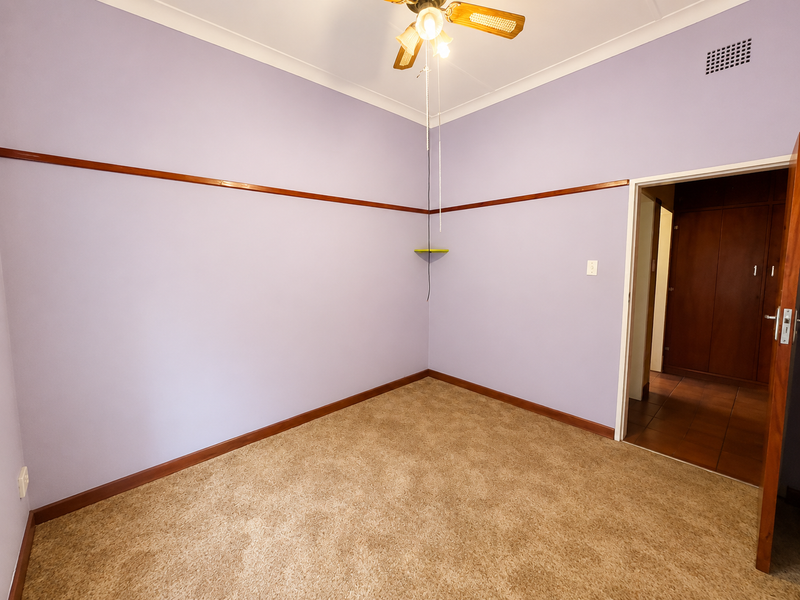 An empty bedroom featuring carpet flooring, a ceiling fan, and a built-in cupboard, with classic picture rail detailing.