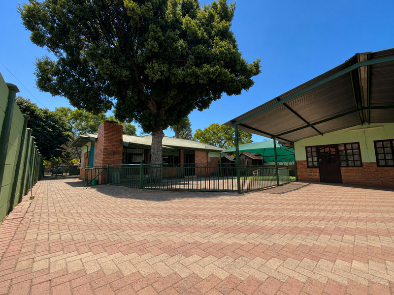 Spacious rear courtyard featuring extensive brick paving, a large covered carport area, and established trees, providing a functional outdoor space.