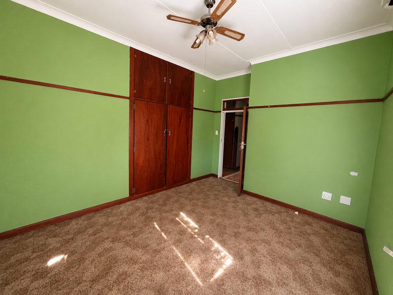 An empty bedroom featuring built-in wooden cupboards, a ceiling fan, and carpeted flooring with a traditional picture rail and coving.