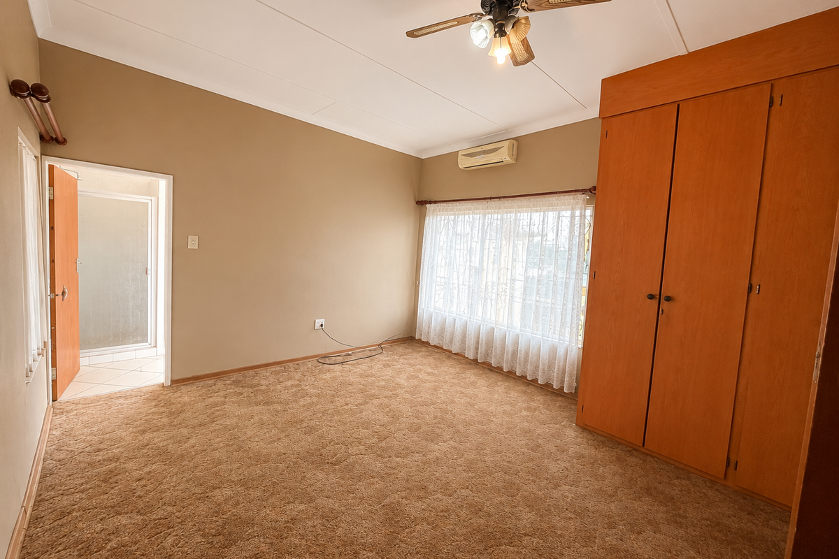 Spacious bedroom featuring built-in wooden cupboards, a ceiling fan, split-system air conditioning, and direct access to an en-suite bathroom.