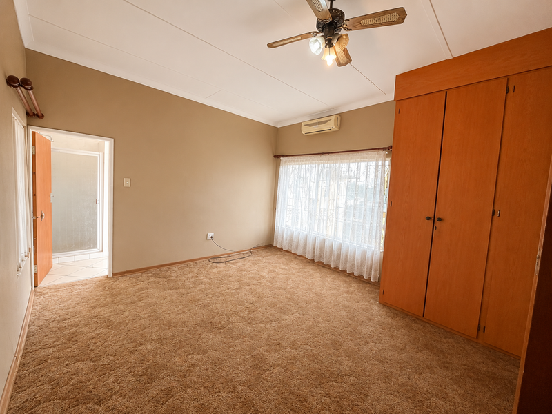 Spacious bedroom featuring built-in wooden cupboards, a ceiling fan, split-system air conditioning, and direct access to an en-suite bathroom.