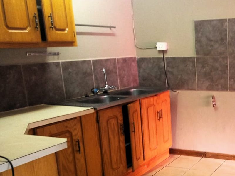 A dated kitchen area featuring wooden cabinetry, a double sink, and tiled splashbacks, currently in need of cosmetic updates and repairs.