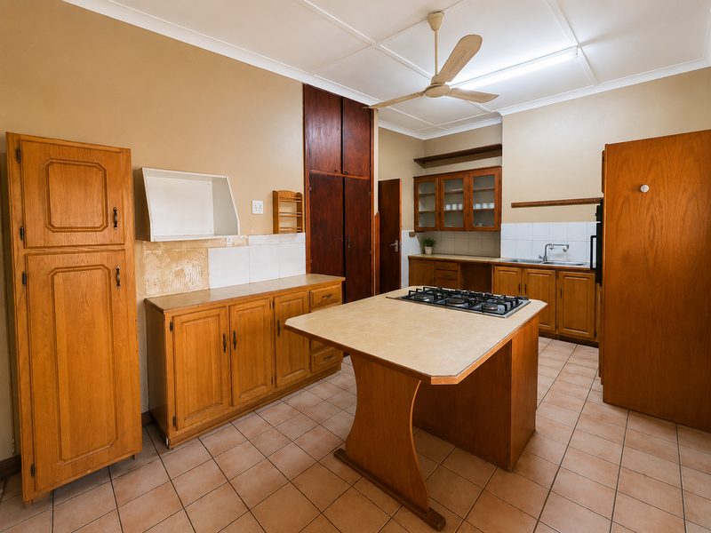 A dated kitchen featuring wooden cabinetry, a central island with a gas cooktop, tiled flooring, and a functional layout ready for modernization.