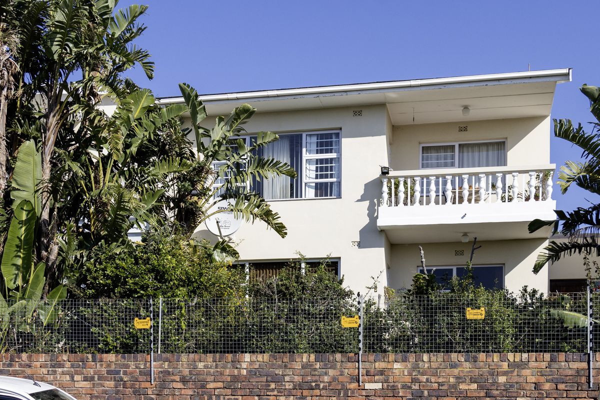 Rear elevation of a two-story townhouse featuring a balcony with balustrade, brick boundary wall with electric fencing, and established garden foliage.