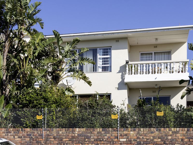 Rear elevation of a two-story townhouse featuring a balcony with balustrade, brick boundary wall with electric fencing, and established garden foliage.