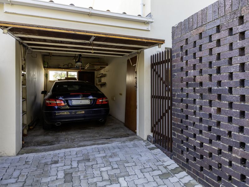 A functional single garage featuring a tilt-up door, paved driveway access, and a decorative brick screen wall providing privacy to the side entrance.