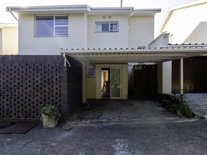 Front exterior view of the townhouse featuring a covered carport, paved driveway, and a decorative brick screen wall at the entrance.